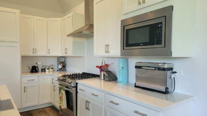 Bright white kitchen with stainless microwave, stove, and toaster on a countertop