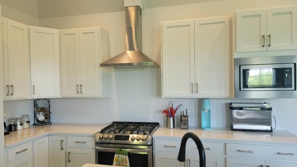Bright white kitchen with stainless steel stove, hood, cabinets, and microwave.