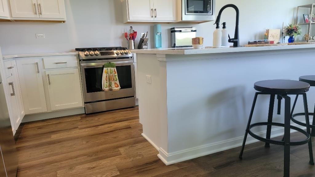 Bright kitchen with white cabinets, wood floors, island counter, and a black stool.