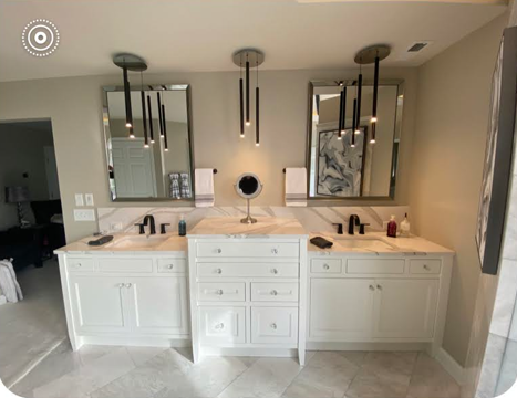 Modern bathroom vanity with two mirrors, white cabinets, and black pendant lights under warm lighting
