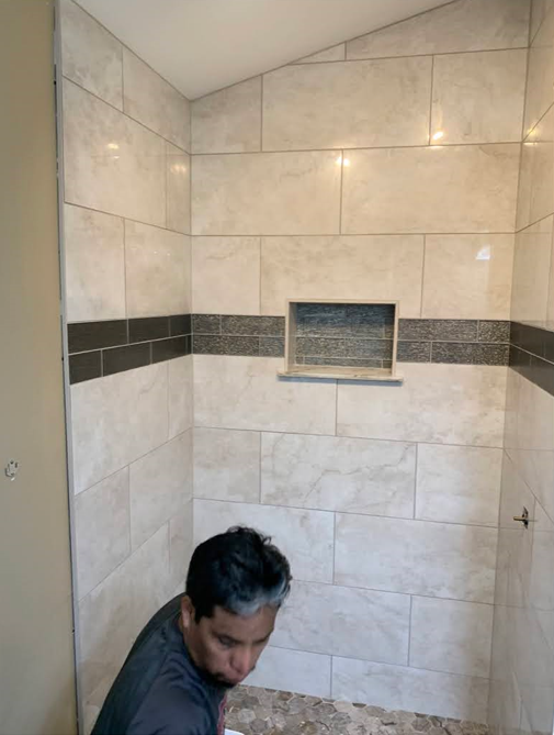 Person in a tiled shower stall, bending down beneath a small window.