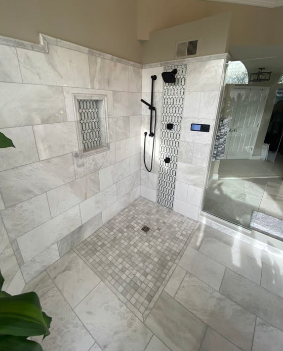 Walk-in tiled shower with glass door, black fixtures, and mosaic floor drain.