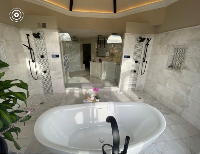 Modern white marble bathroom with a freestanding oval tub, walk-in shower, and warm ceiling lighting