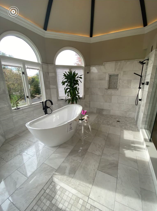 Bright marble bathroom with a freestanding tub, arched windows, and walk-in shower
