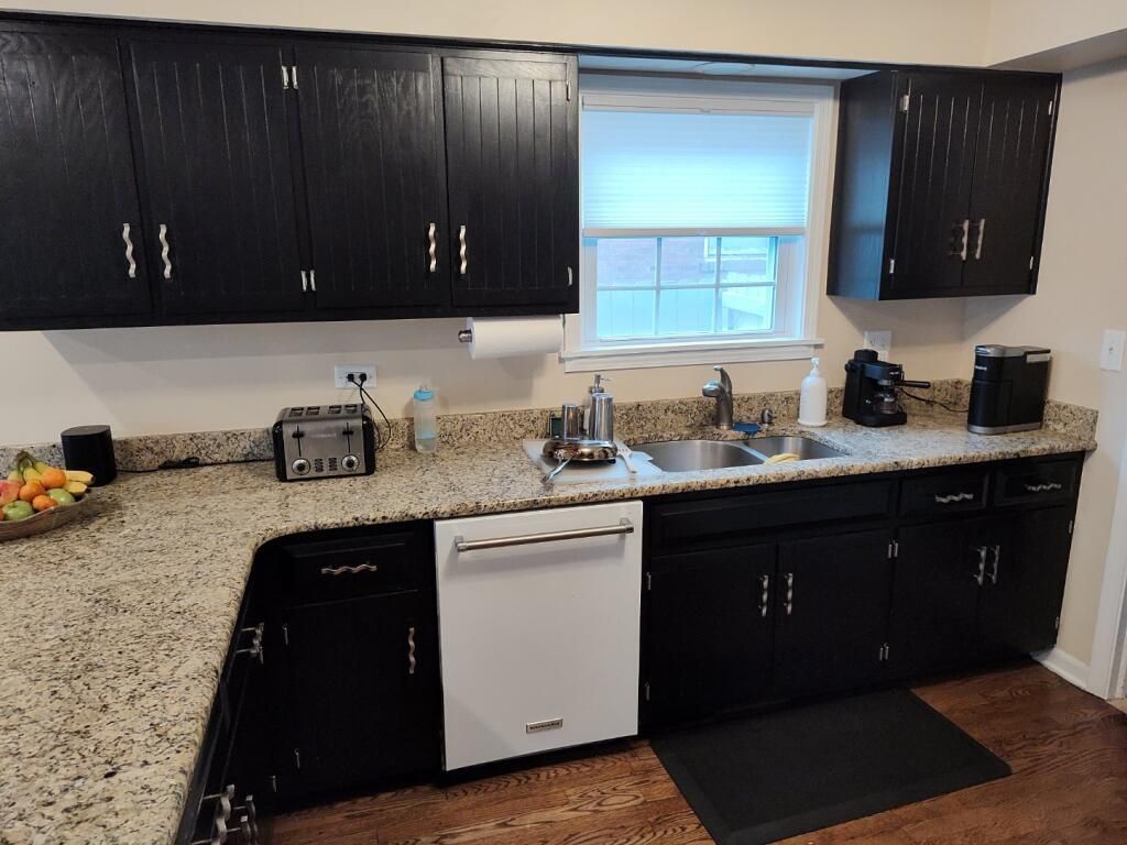 Modern kitchen with dark cabinets, speckled counters, white dishwasher, and a window over the sink.