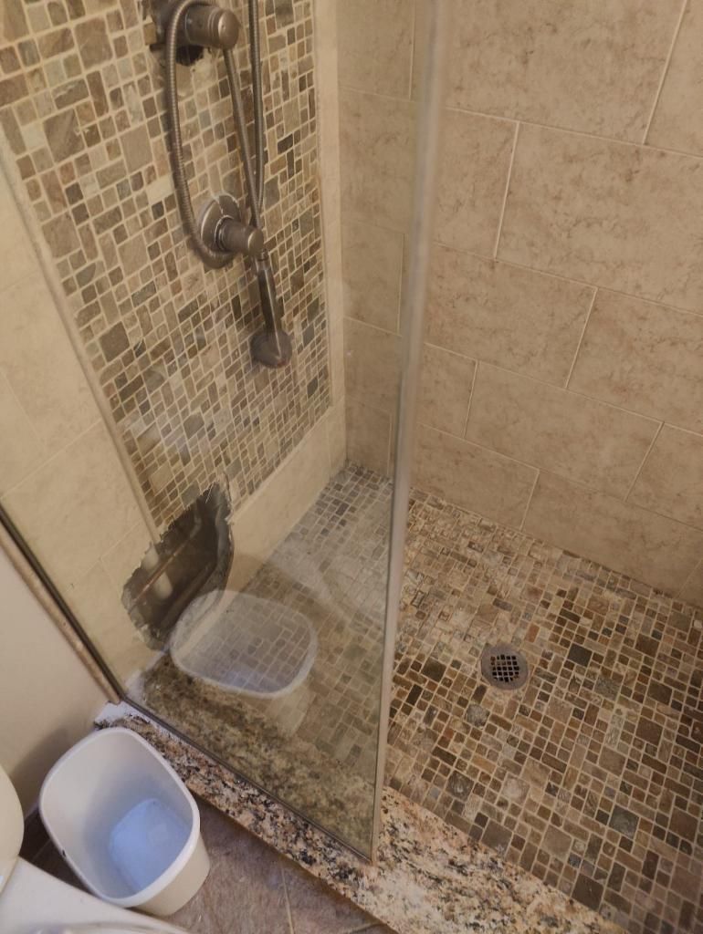 Small tiled shower with glass partition, showerhead, drain, and two buckets on the floor.