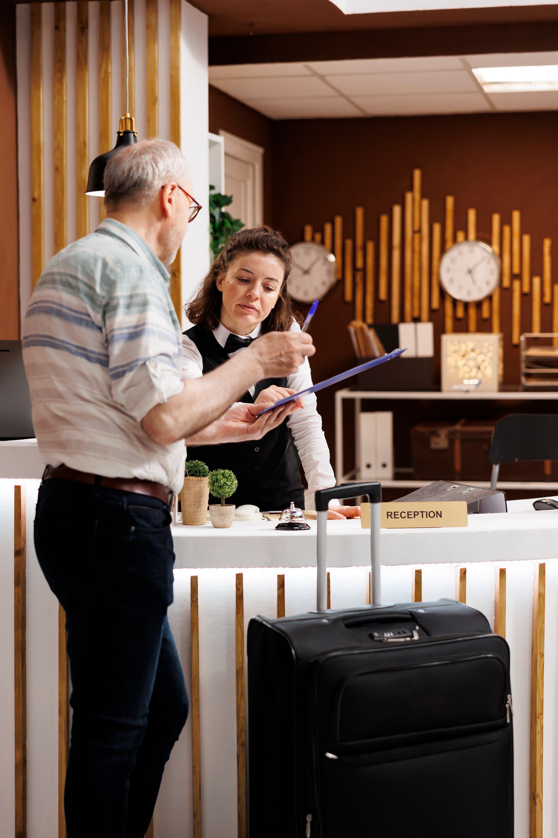 Hombre en la recepción del hotel con asistente, realizando el check-in. El equipaje se encuentra cerca.