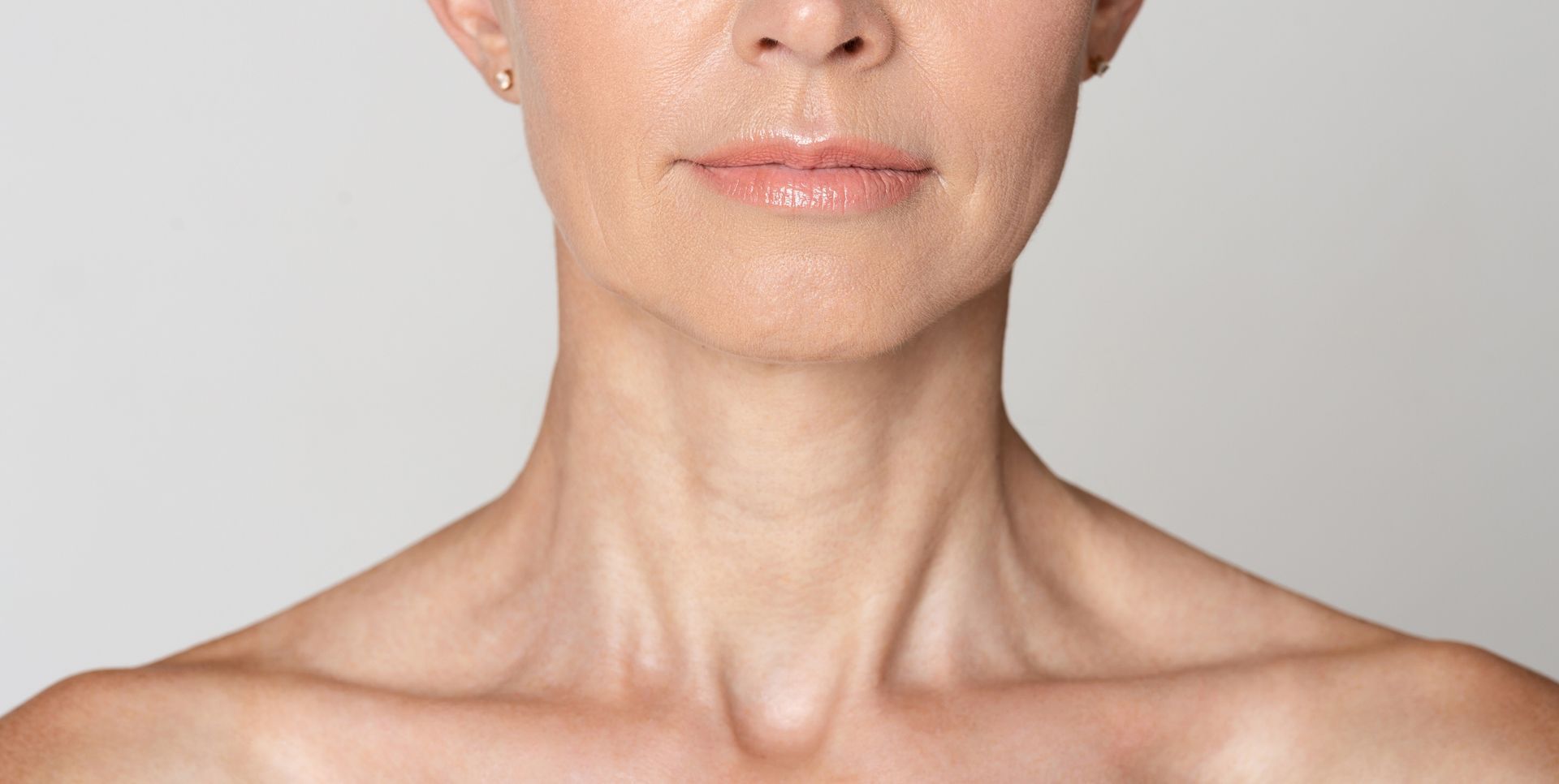 Close-up of a person’s lower face, neck, and shoulders against a light gray background.