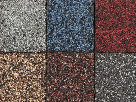 Close-up of six asphalt roofing shingles in various speckled colors: gray, blue, red, brown, burgundy, and dark gray.