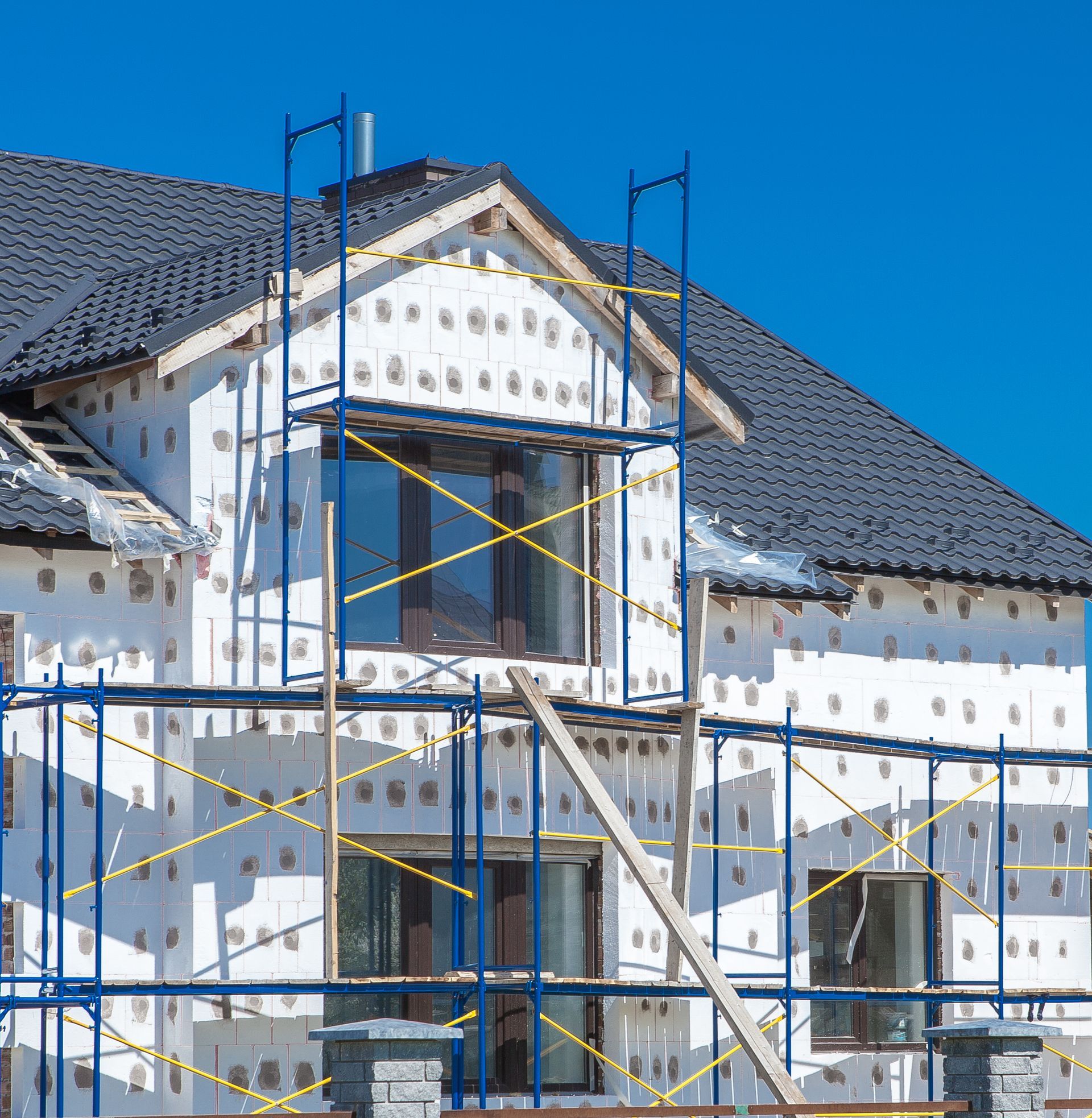 A house under construction with white insulation panels on the exterior walls and blue metal scaffolding around it.