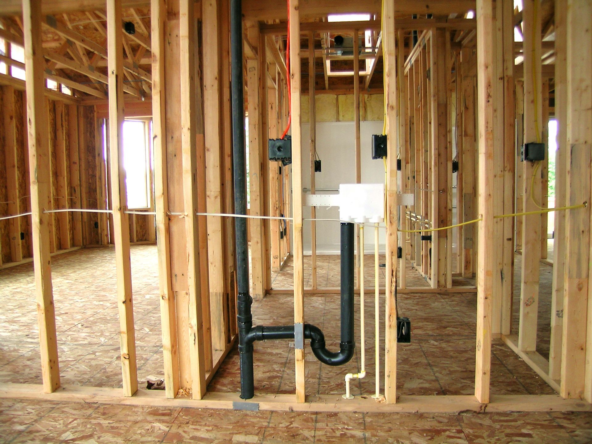 La structure intérieure d'une maison en construction, montrant les tuyaux de plomberie et le câblage électrique à l'intérieur des montants muraux en bois.