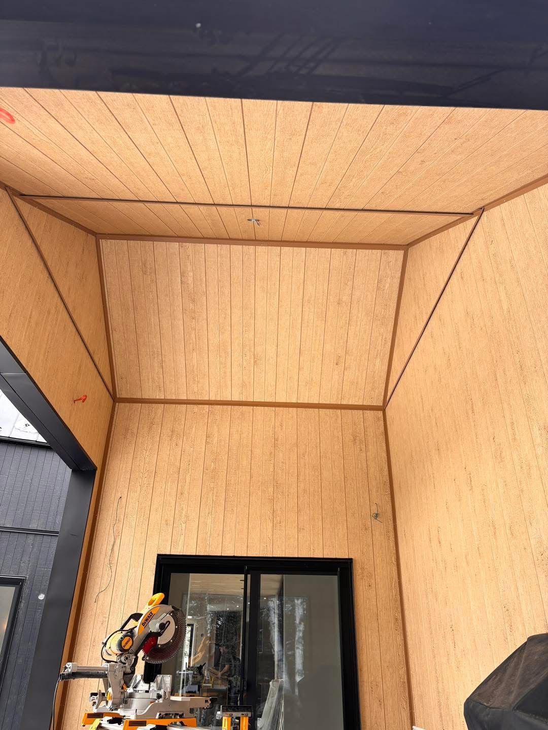 Vue en contre-plongée d'un plafond et de murs de véranda recouverts de lambris en bois clair à rainures verticales.