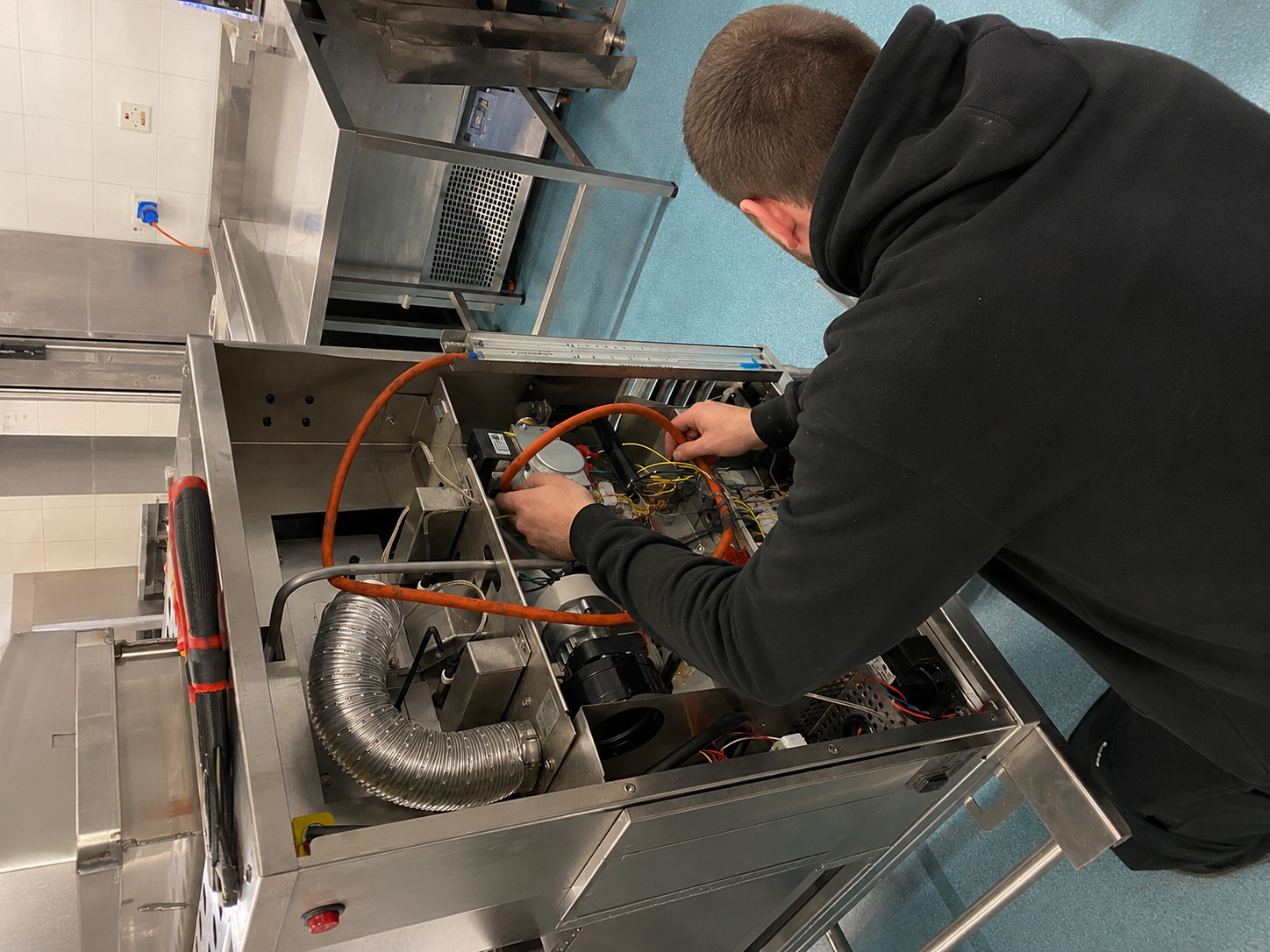 Technician working inside an open machine, using orange hoses in an industrial workspace