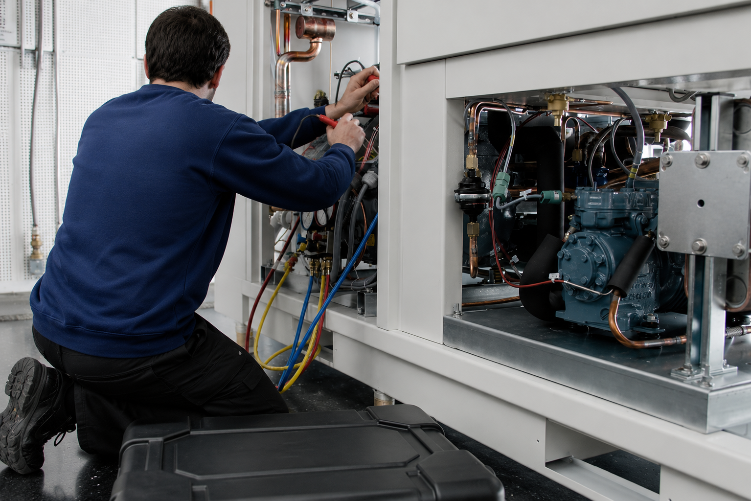 Technician kneels beside an open industrial machine, adjusting cables and components in a lab setting