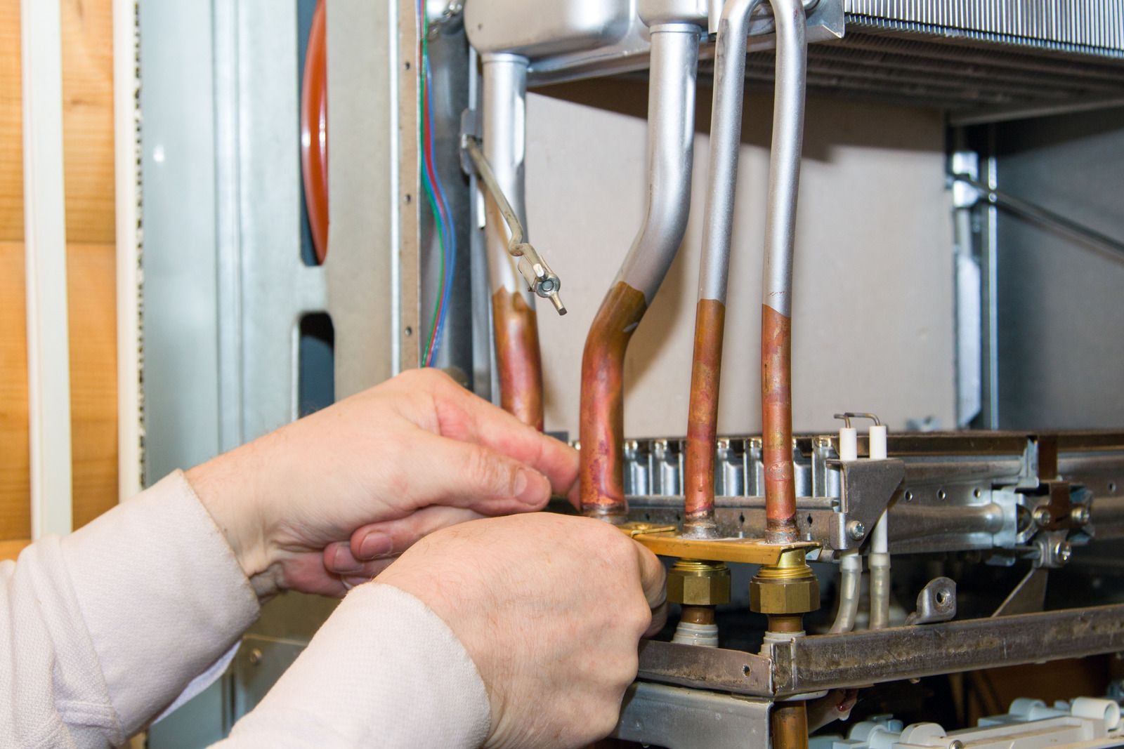 Hands adjusting copper pipes and a brass valve inside an industrial machine