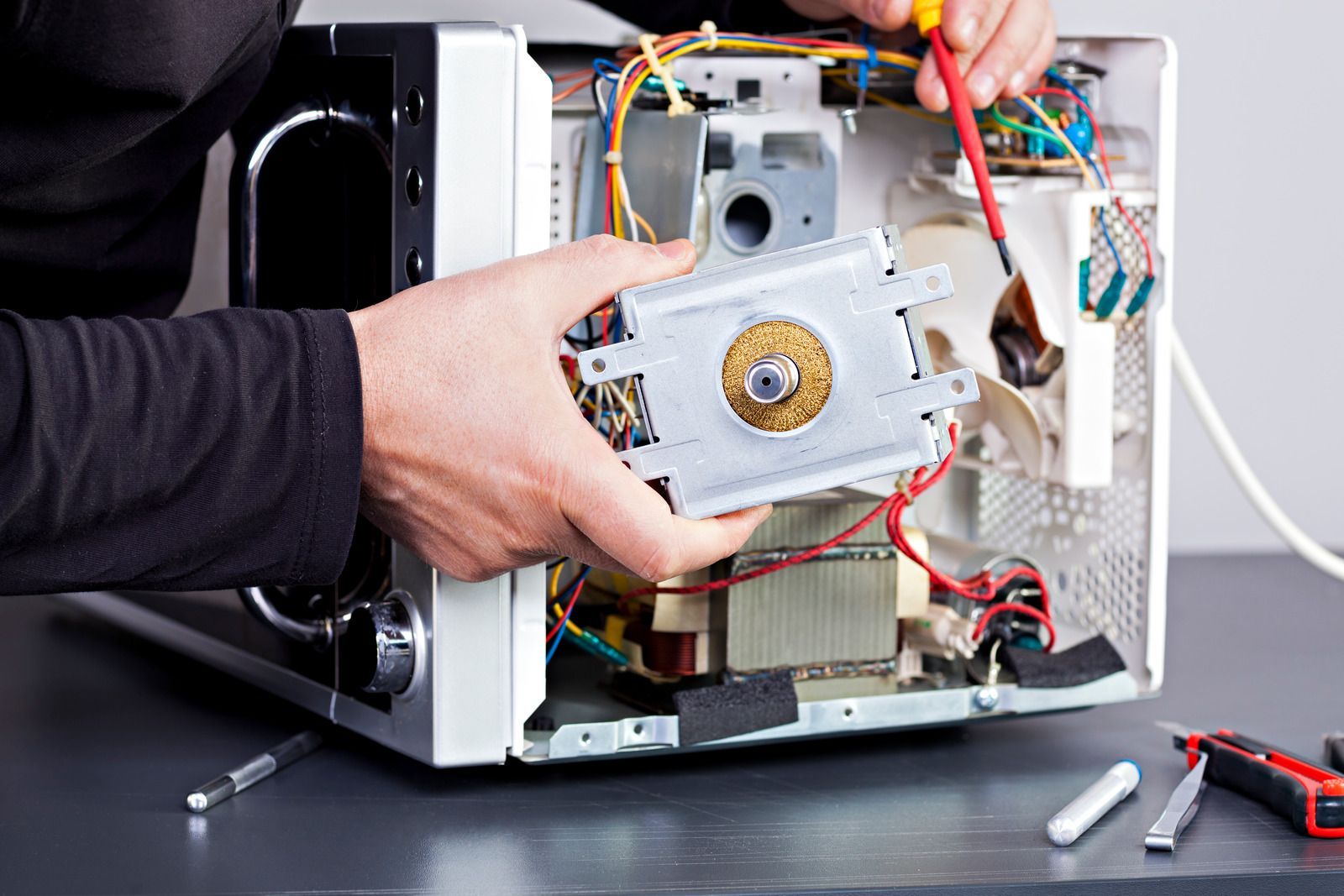 Hands removing a metal component from an electronic device with wires exposed on a workbench