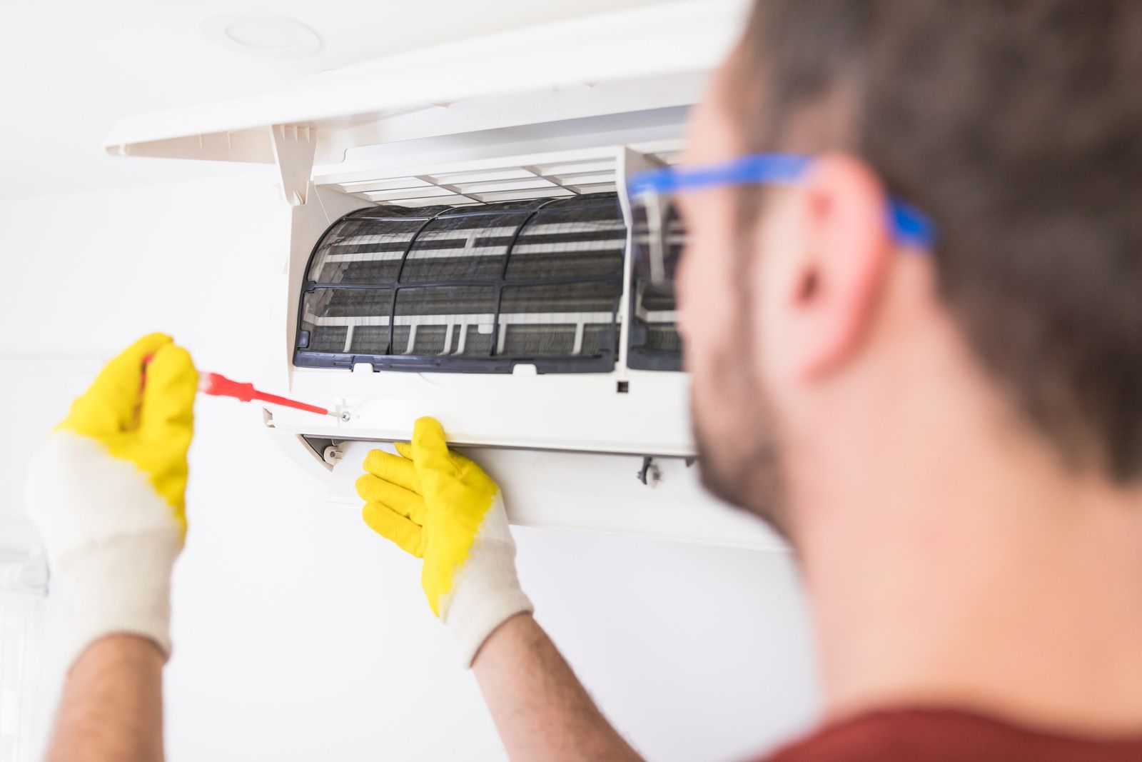 Technician cleaning a wall-mounted air conditioner with a brush and cloth