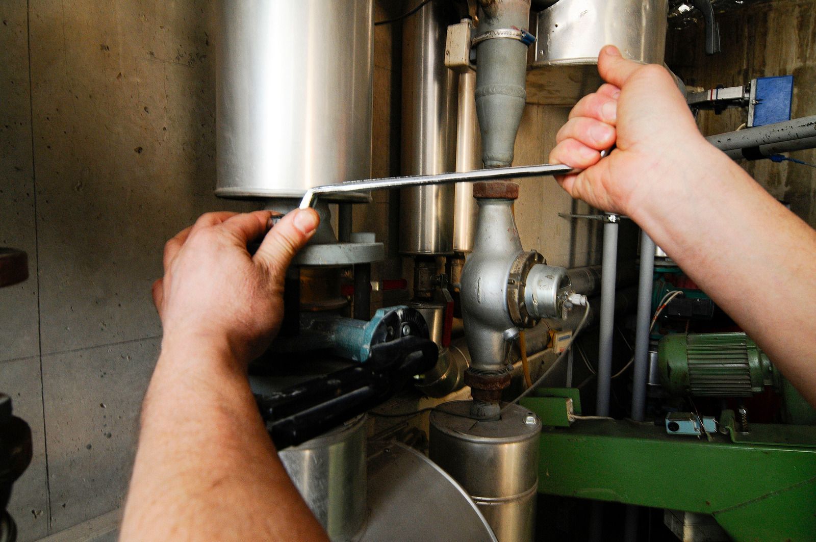 Hands using a wrench to tighten a pipe in an industrial machine room