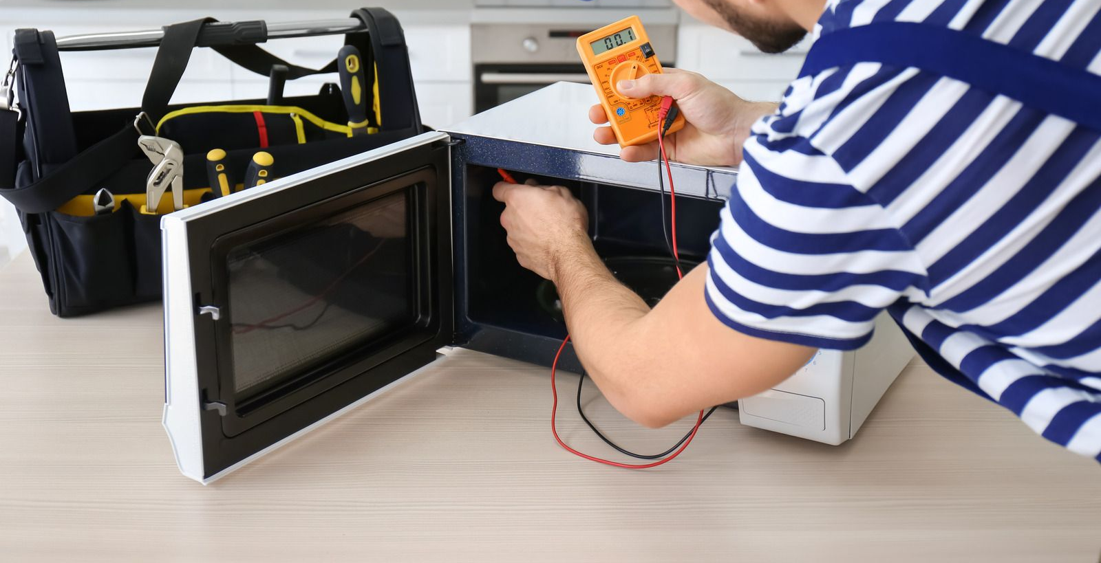 Person using a multimeter to test wiring on an open electronic device on a table