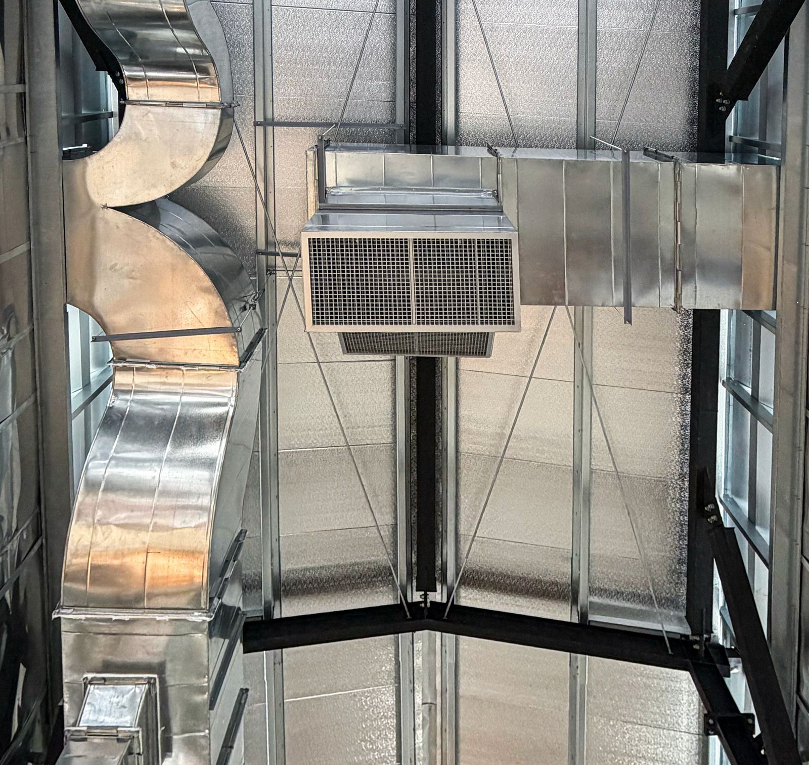 Industrial ceiling with silver ductwork, mesh panels, and a central ventilation unit.