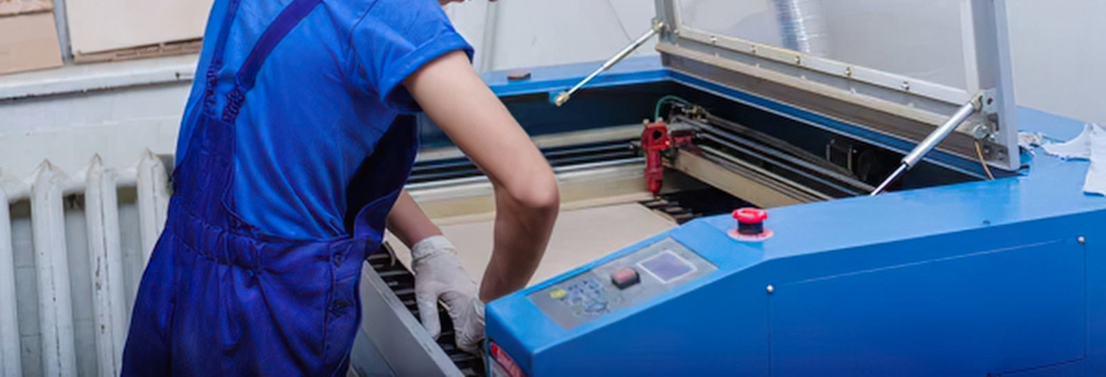 Person in blue shirt operating a blue industrial machine with an open lid.