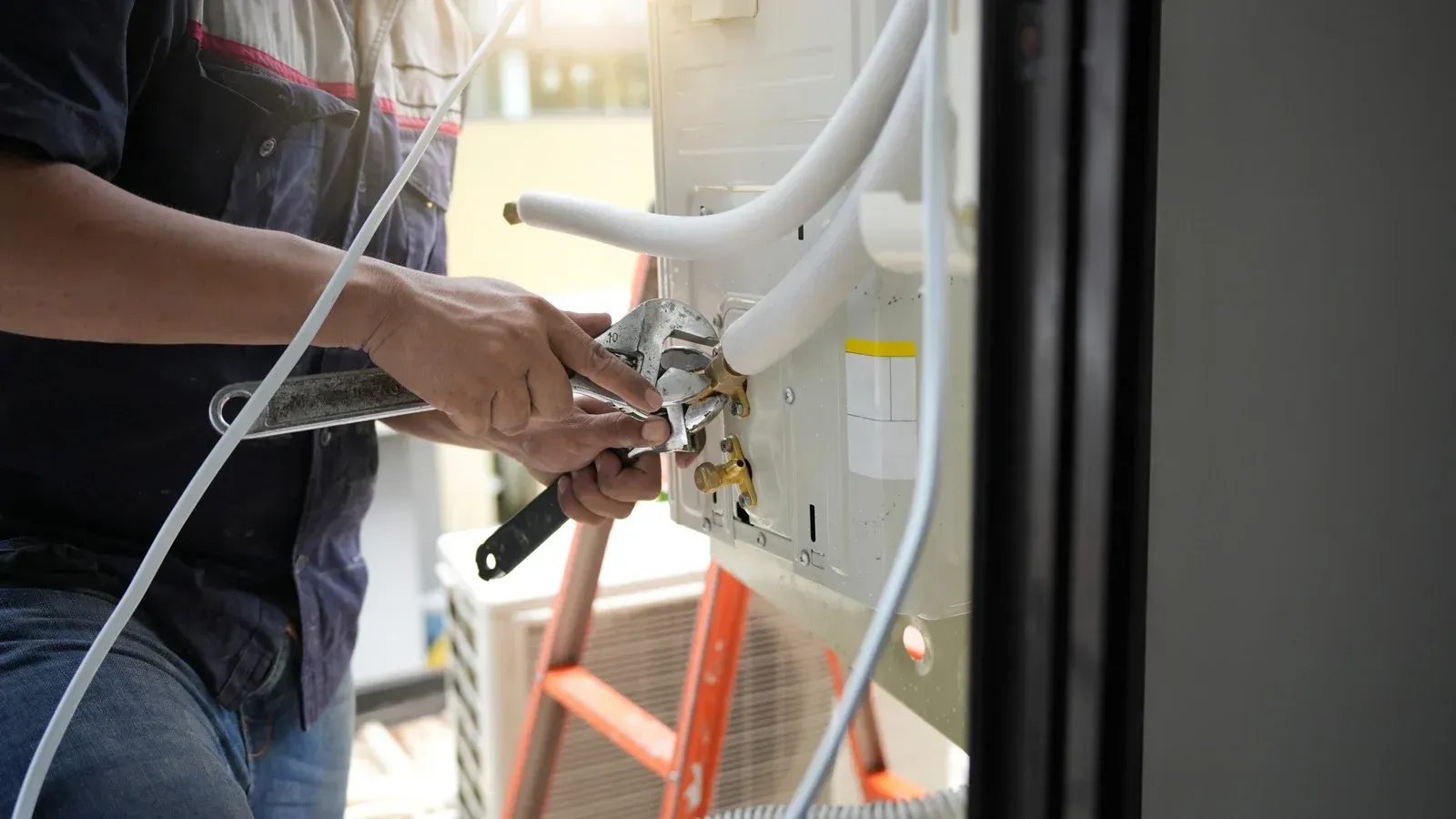 Technician using tools to service outdoor air conditioning unit with white hoses attached