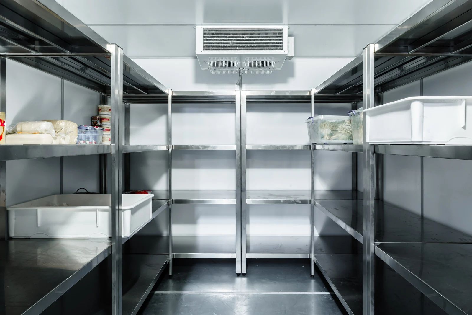 Empty stainless-steel walk-in refrigerator with metal shelving and storage bins