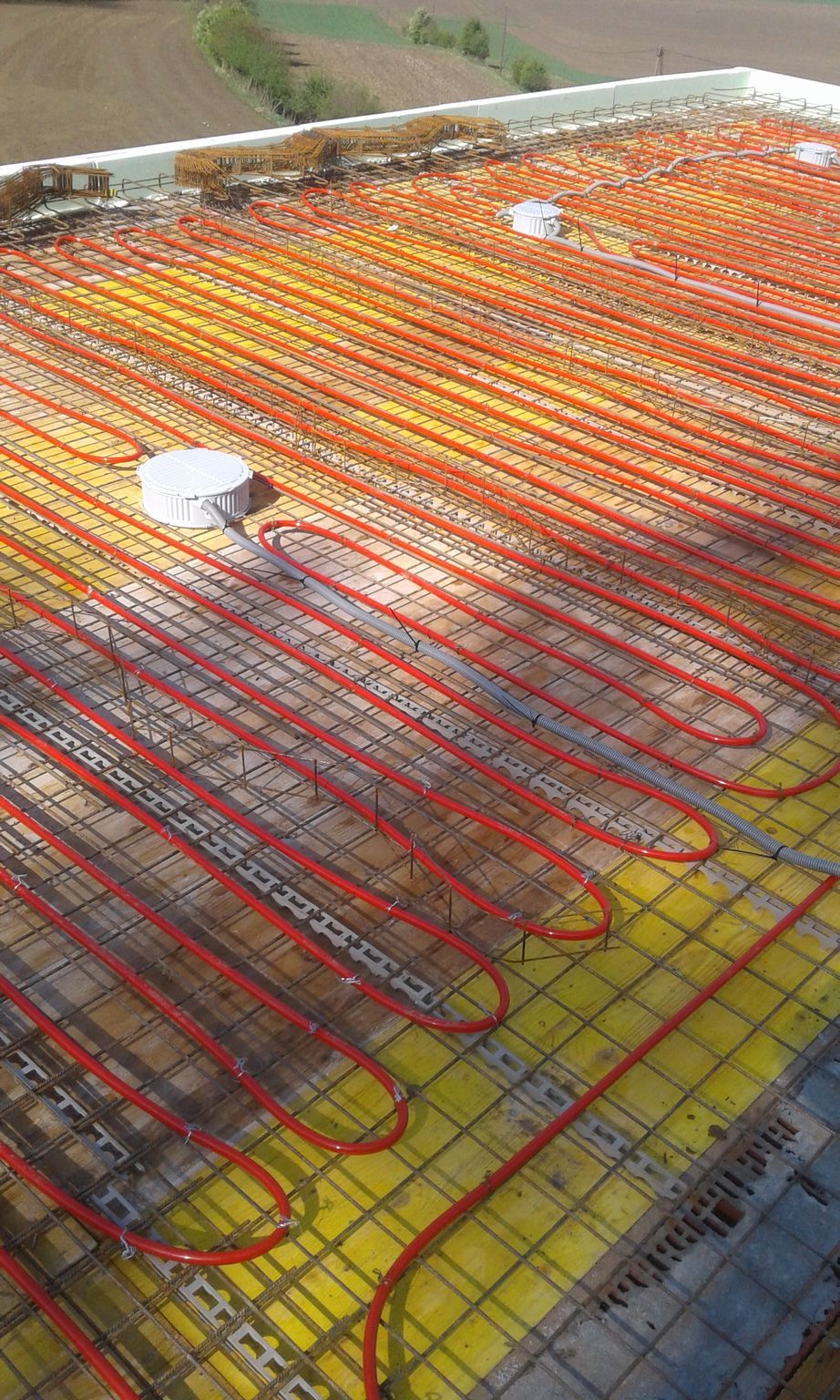 Rote Fußbodenheizungsrohre auf einer Betonplatte verlegt, gelbe Isolierung sichtbar.