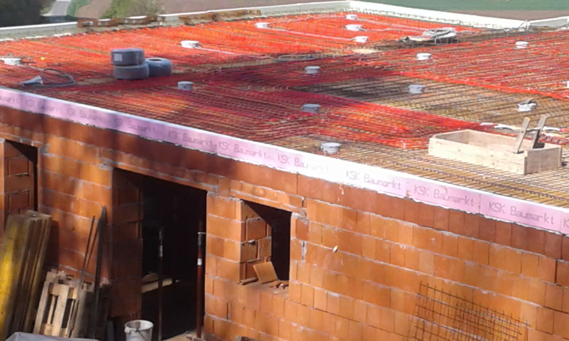 Rohbau eines Hauses, das mit rotem Drahtgeflecht bedeckt ist und auf Betonstützen steht.