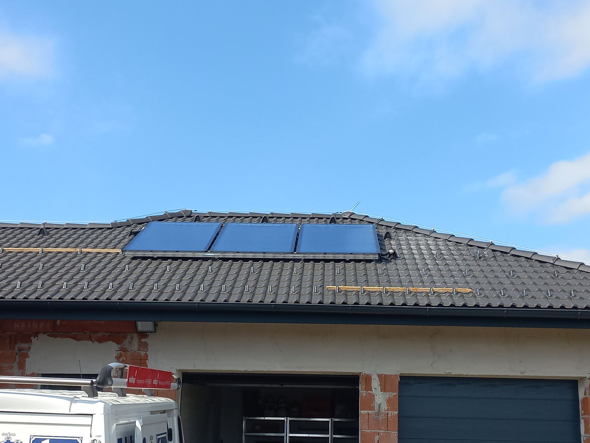Solarpaneele auf einem Ziegeldach über einer Garage unter blauem Himmel.