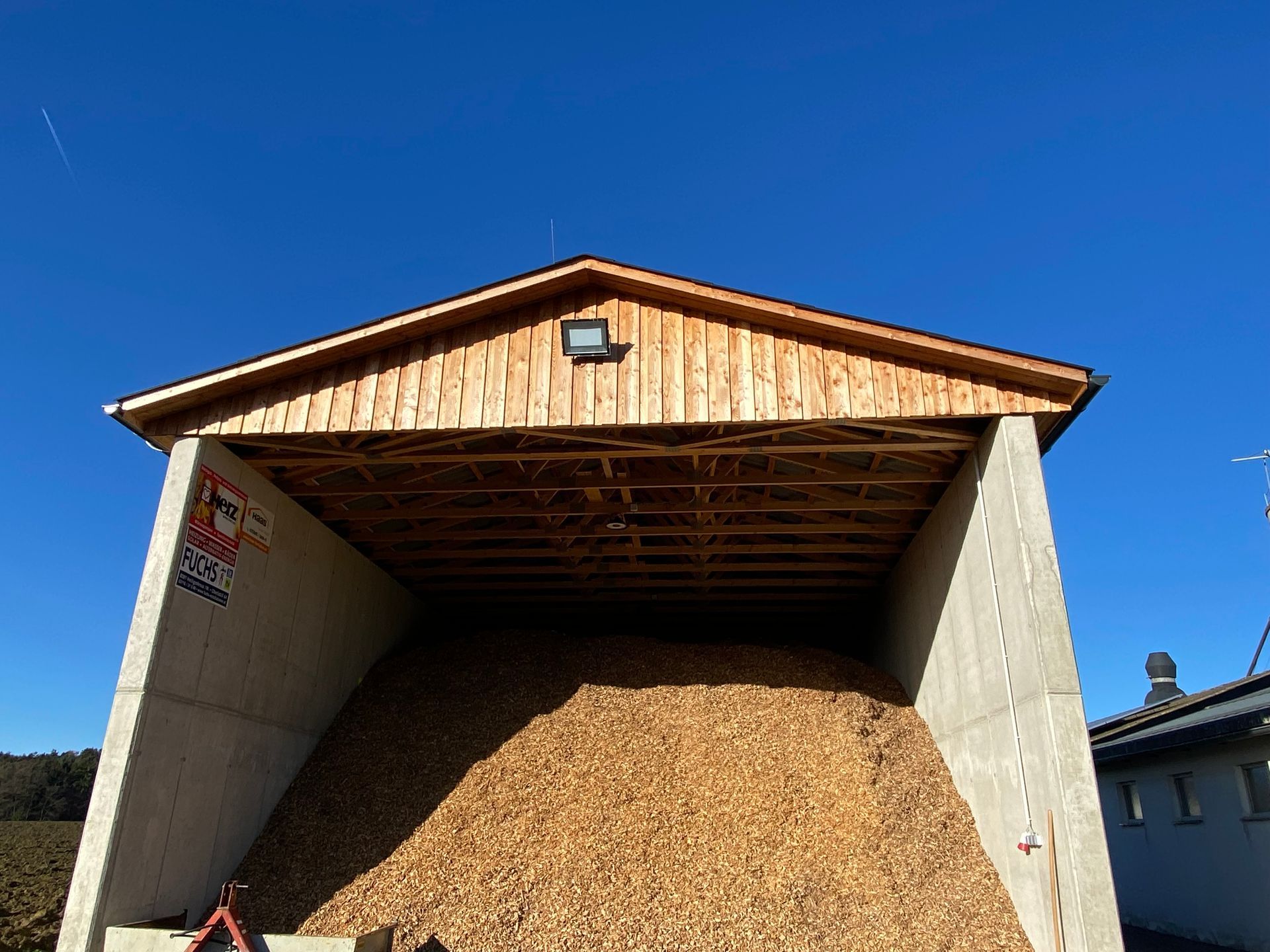 Holzspänelager mit Holzdach, Betonwänden und blauem Himmel.