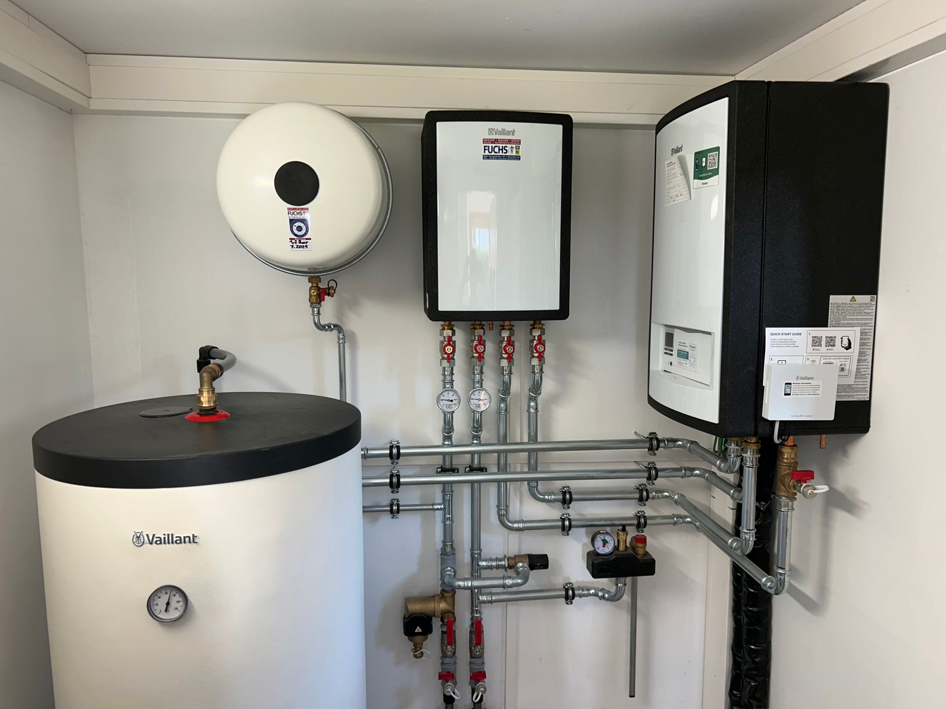 Drei Warmwasserbereiter und die dazugehörigen Rohrleitungen in einem Hauswirtschaftsraum.