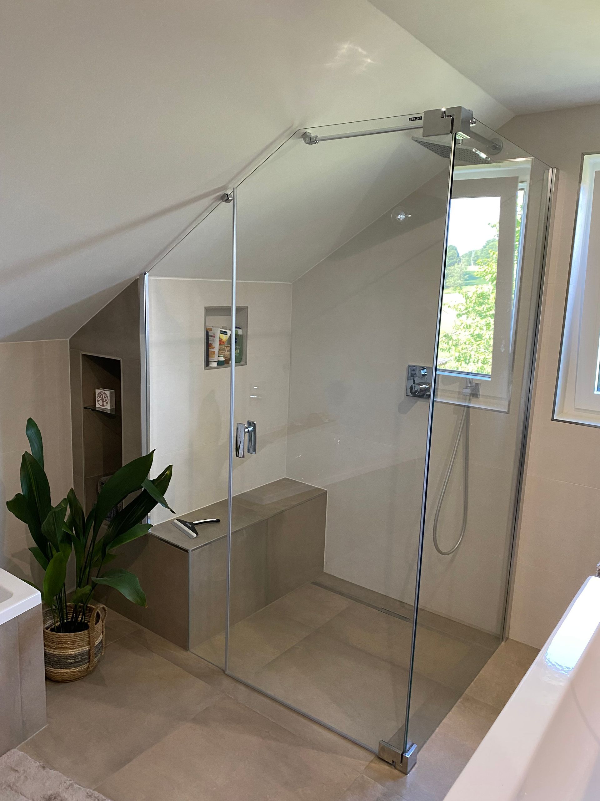 Modernes Badezimmer mit Glasdusche im Dachgeschoss. Beige Fliesen, Sitzbank und Topfpflanze.