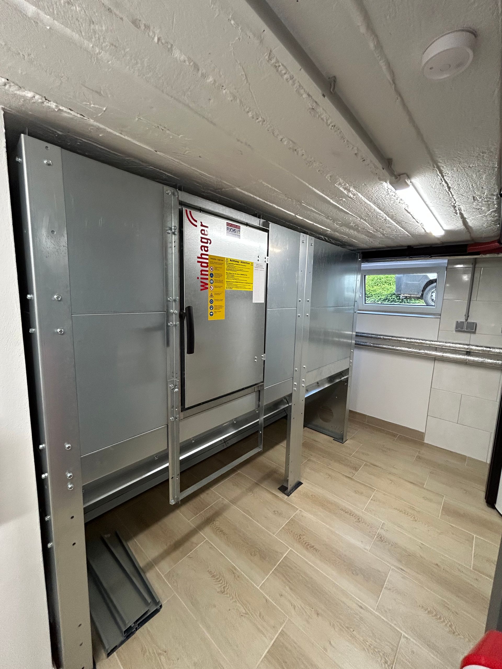 Metallener Hauswirtschaftsraum mit einem großen Schrank und einer im Hintergrund sichtbaren kleinen Küche.