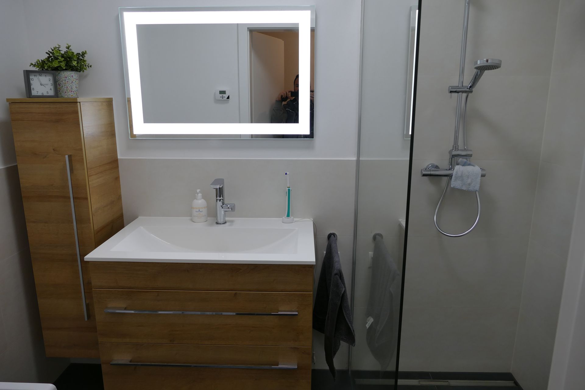 Badezimmer mit Waschtisch aus Holz, beleuchtetem Spiegel und Glasdusche.