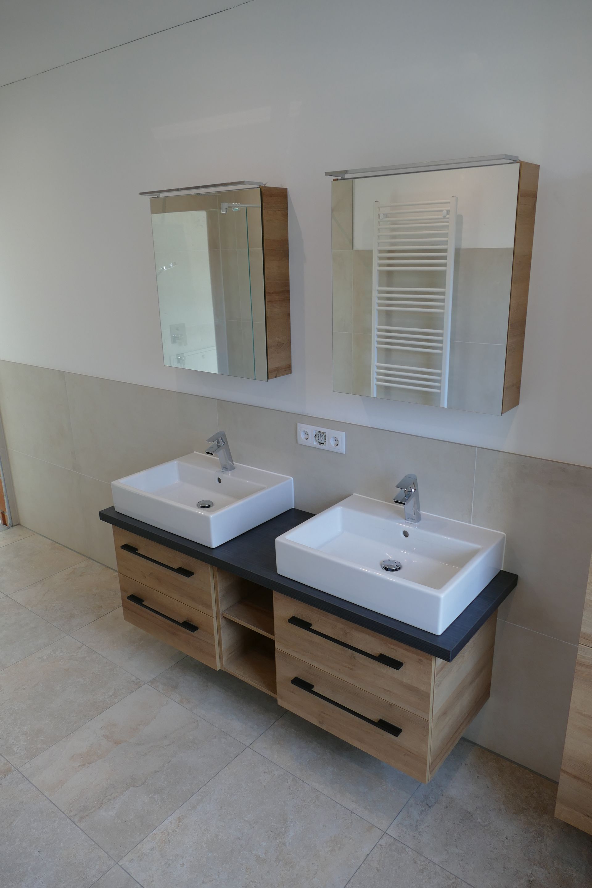 Badezimmer mit zwei weißen, quadratischen Waschbecken auf einem Holz-Waschtisch. Darüber ist ein Spiegel.
