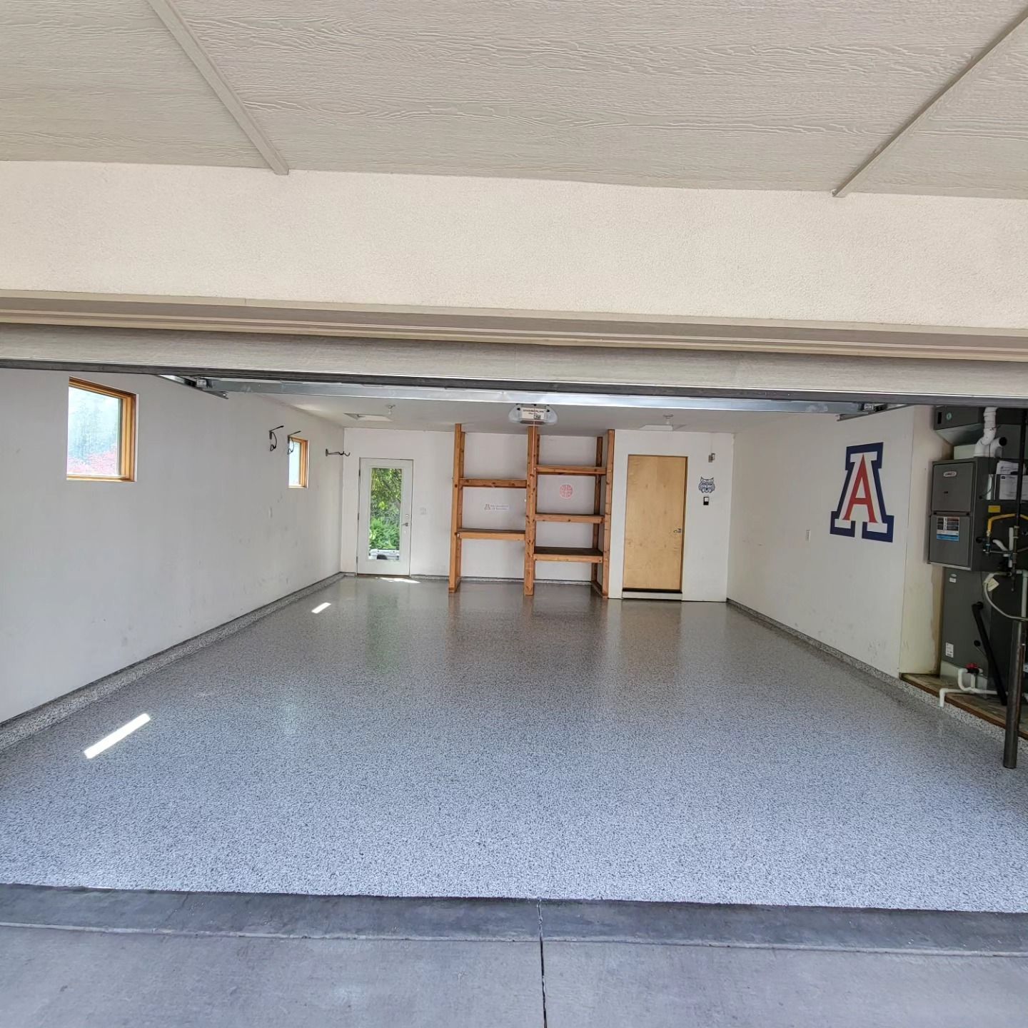 Empty garage with gray epoxy floor, white walls, shelves, and a wooden door at the back.