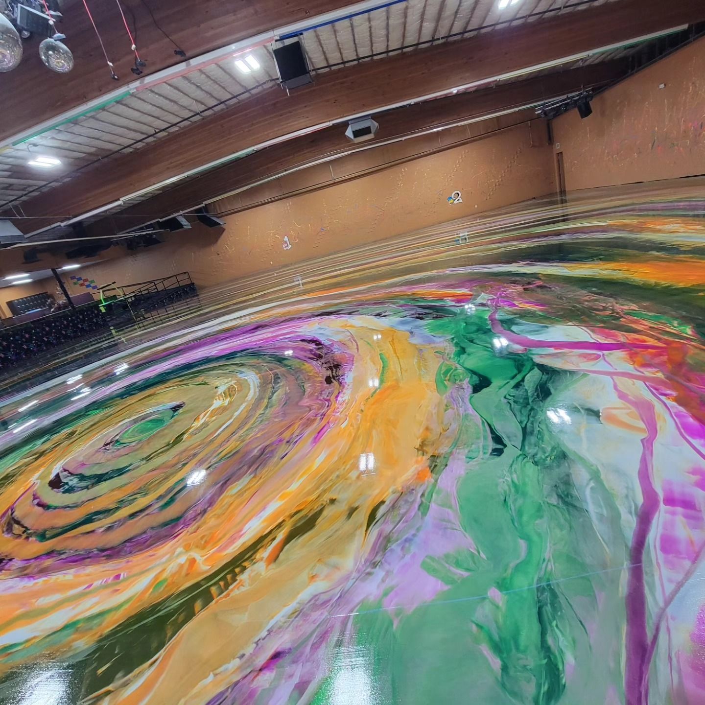 Abstract swirl of colorful paint spreading across a gym floor beneath a wooden ceiling
