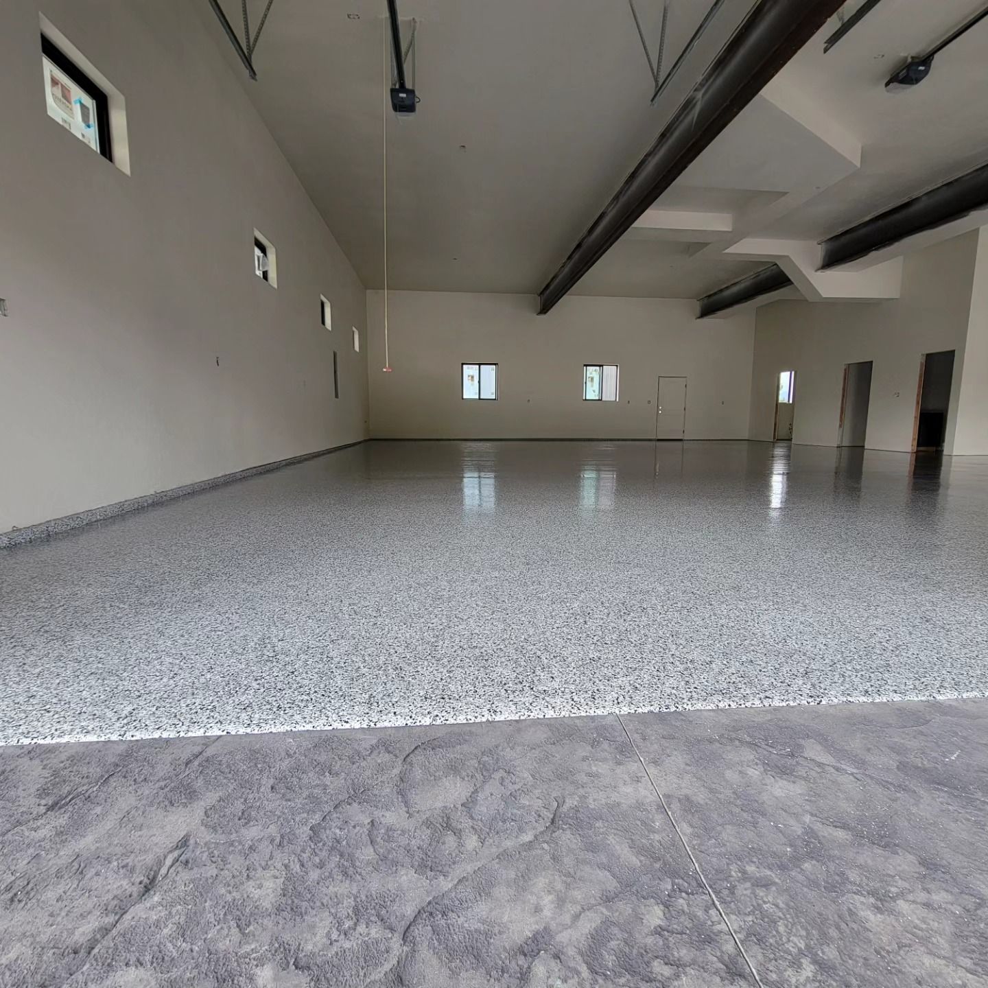 Empty garage interior with gray speckled floor, white walls, and small windows.