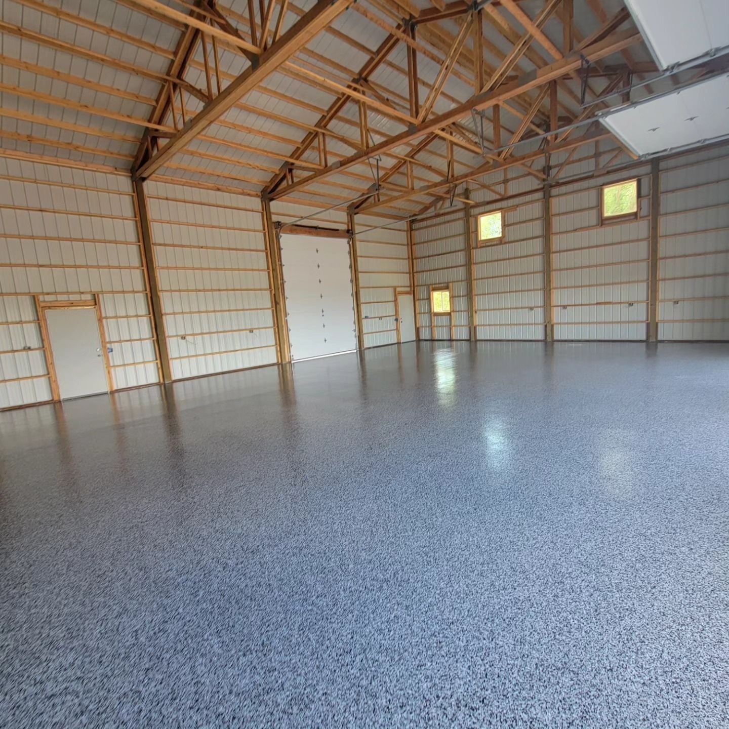 Empty metal workshop interior with exposed wood trusses and a polished gray concrete floor