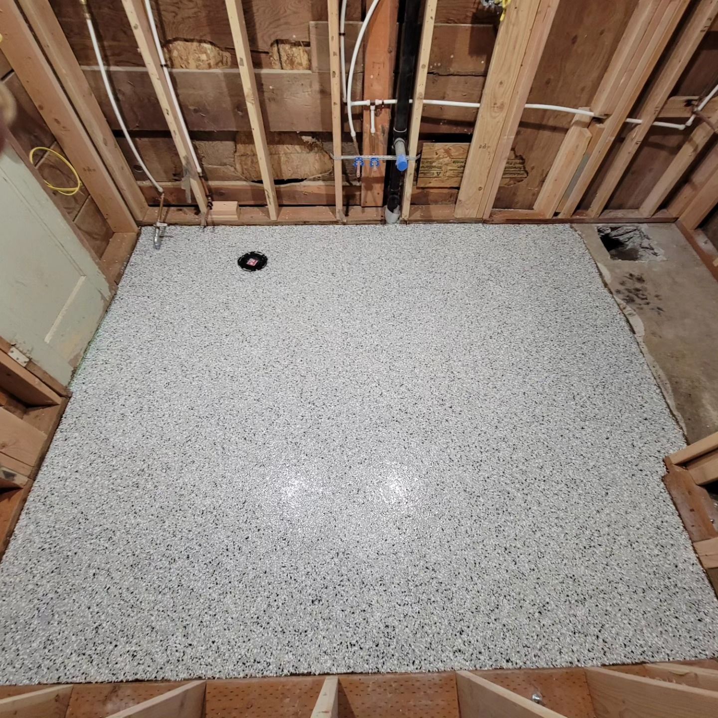 Bathroom subfloor with speckled tile floor and exposed wall framing during renovation
