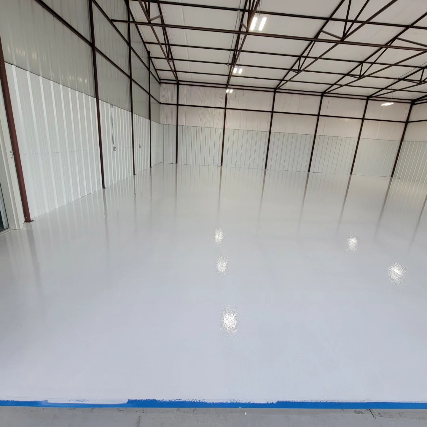 Empty white-floored warehouse interior with metal walls and ceiling beams