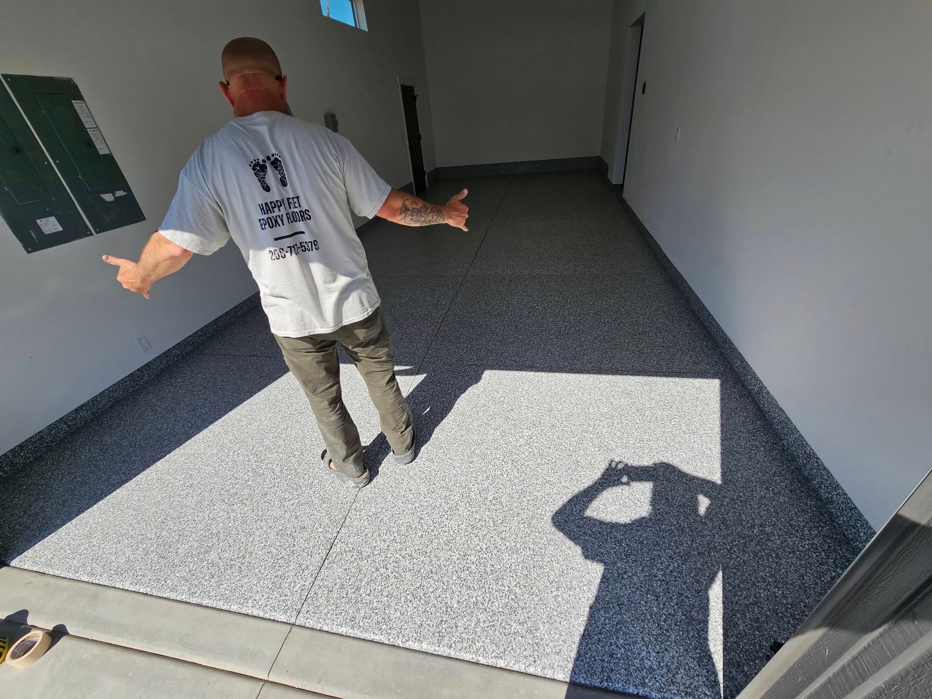 Person standing in a sunlit hallway beside a gray textured floor mat, arms outstretched.