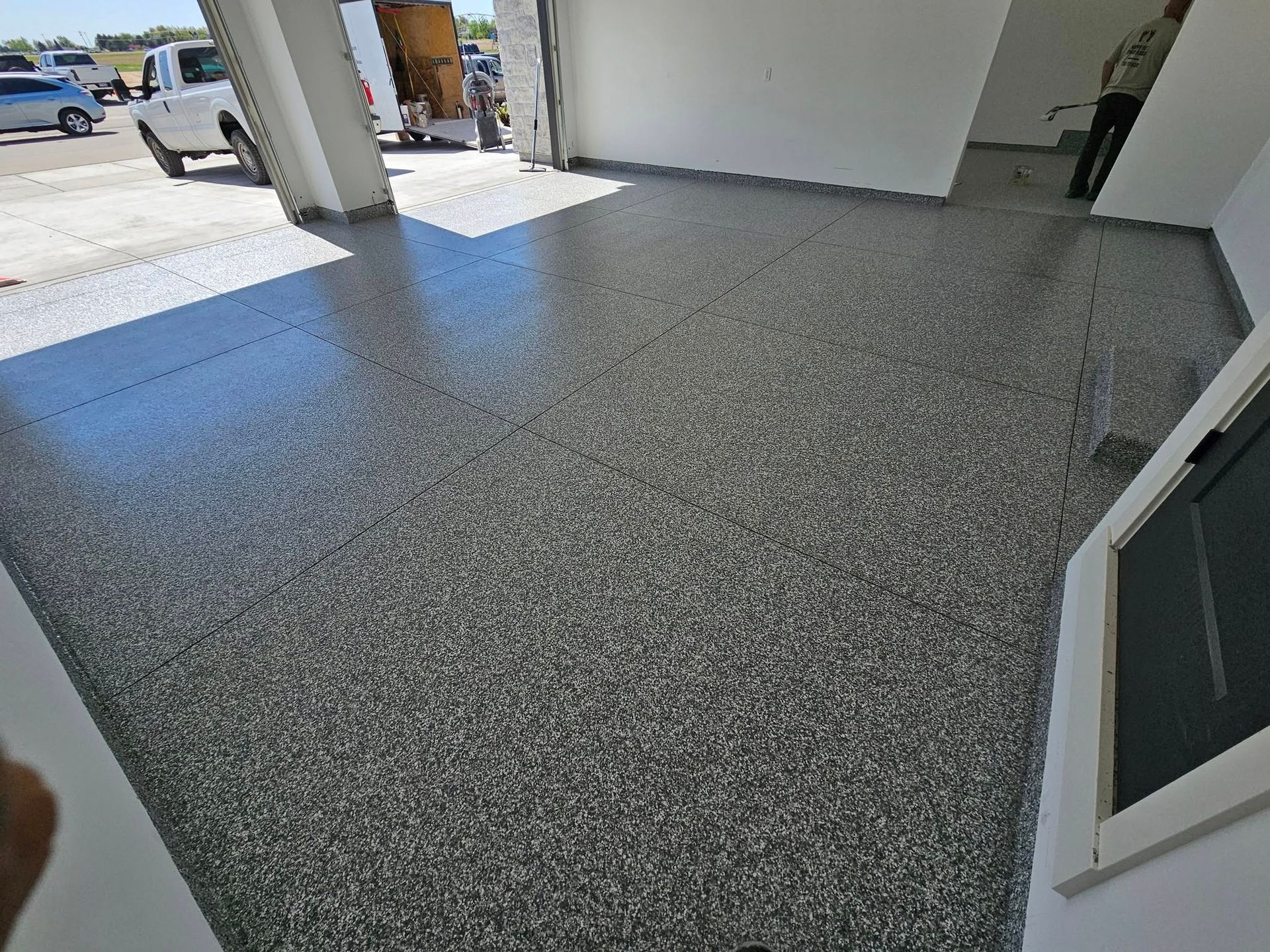 Empty gray speckled floor in a bright garage or showroom with an open doorway to outside