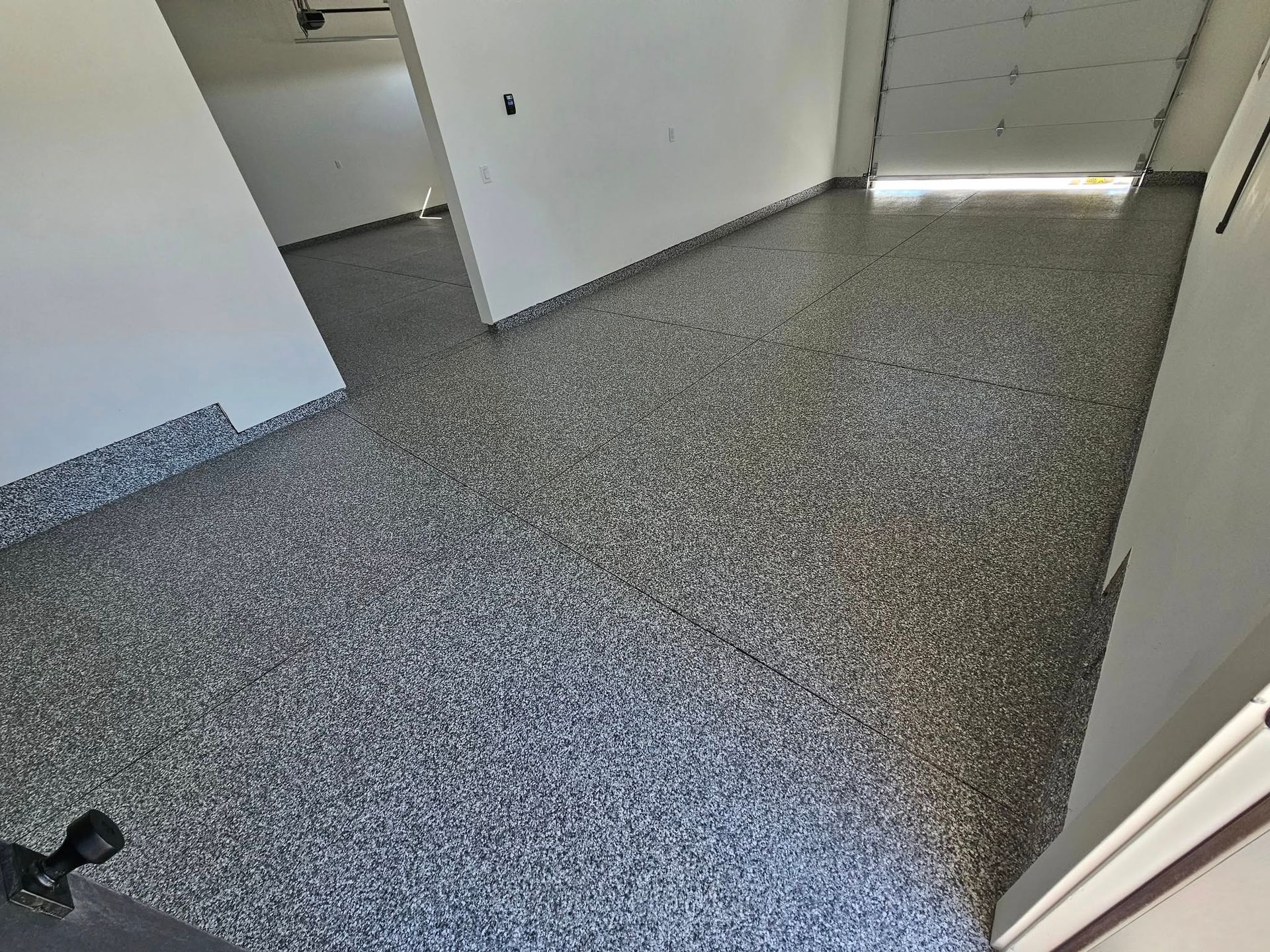 Empty garage with gray speckled floor and white walls, viewed from a doorway