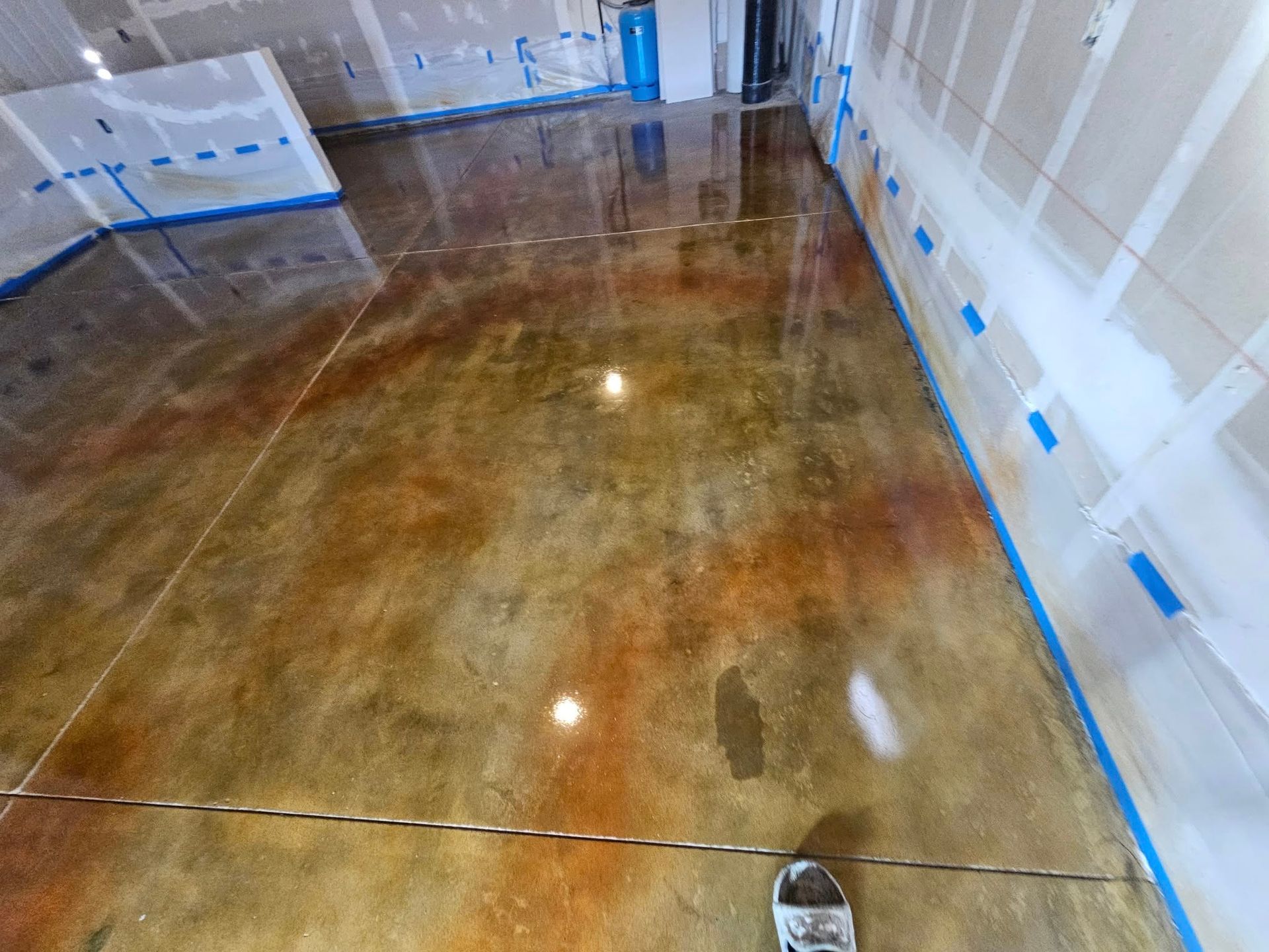 Polished concrete floor in a room under renovation, with plastic-covered walls and blue painter’s tape.