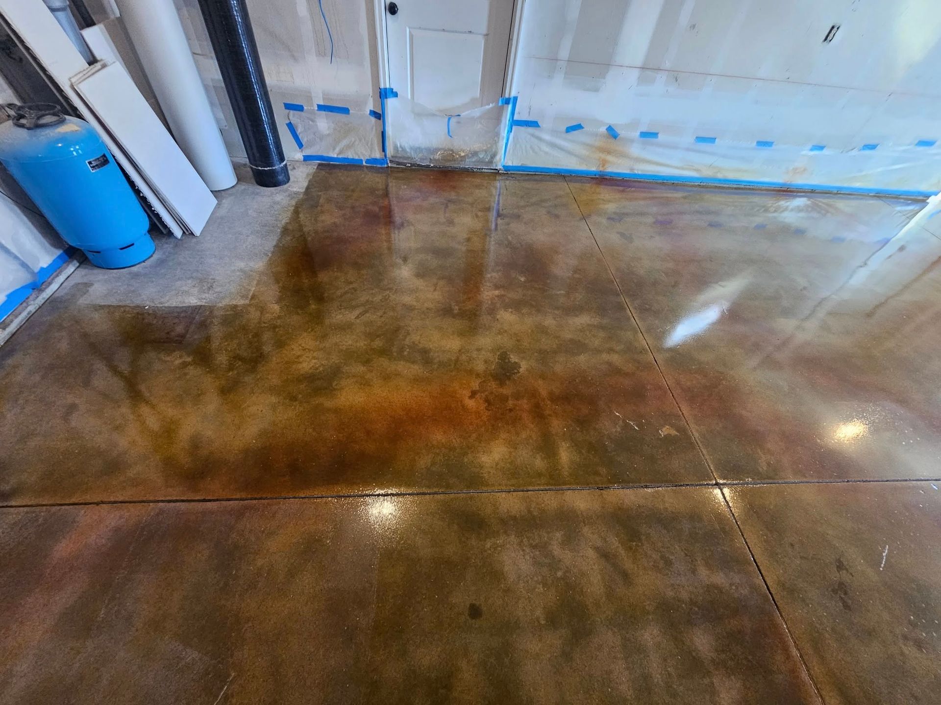 Shiny brown concrete floor in an industrial room with blue wall tape and a blue barrel