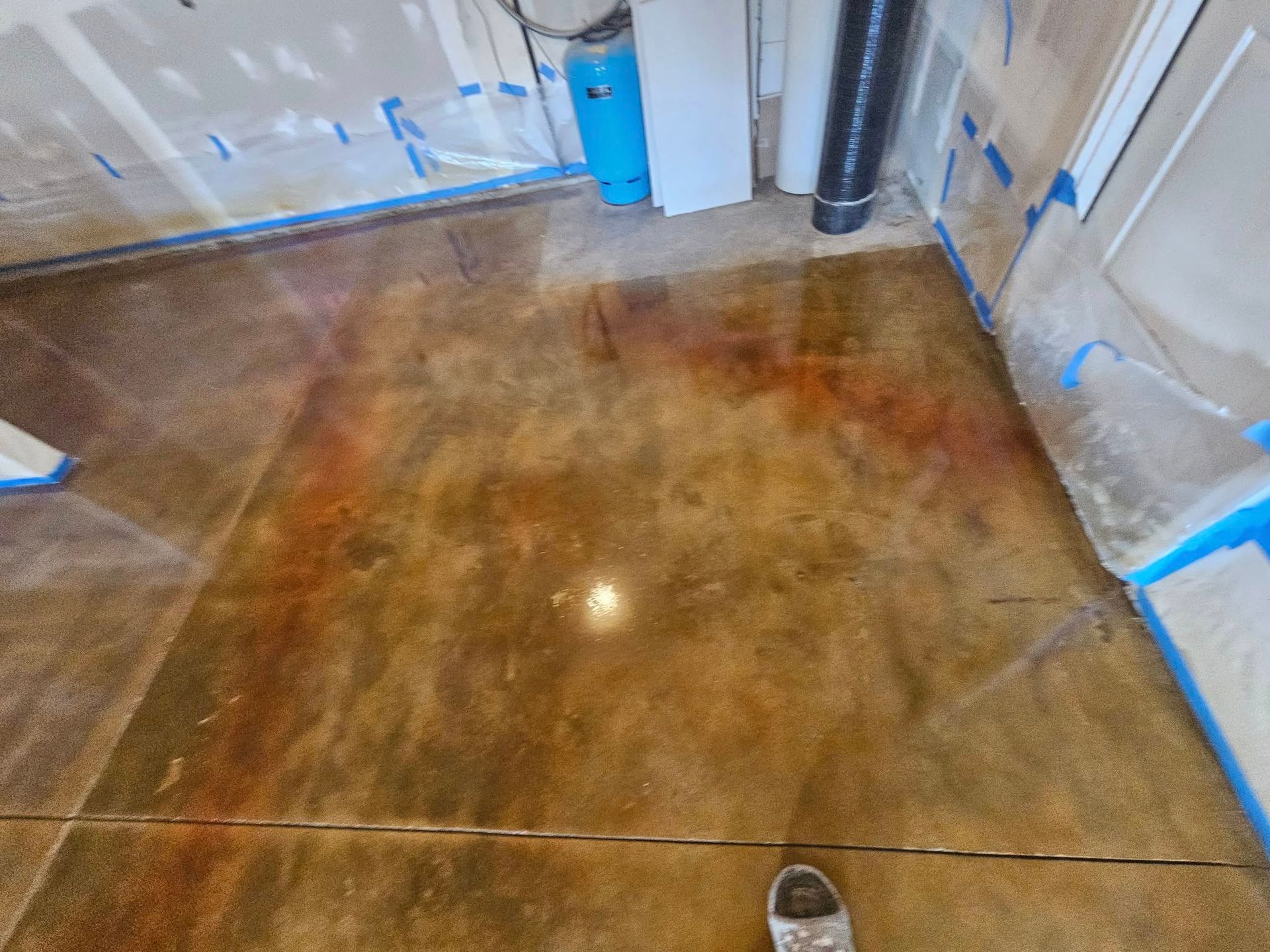 Stained concrete floor in a garage or basement with blue painter’s tape along the walls.