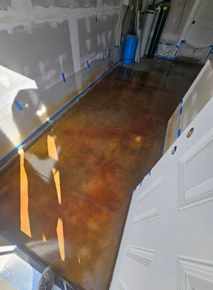 Freshly coated brown concrete floor in a hallway under renovation, with unfinished walls and a blue container.