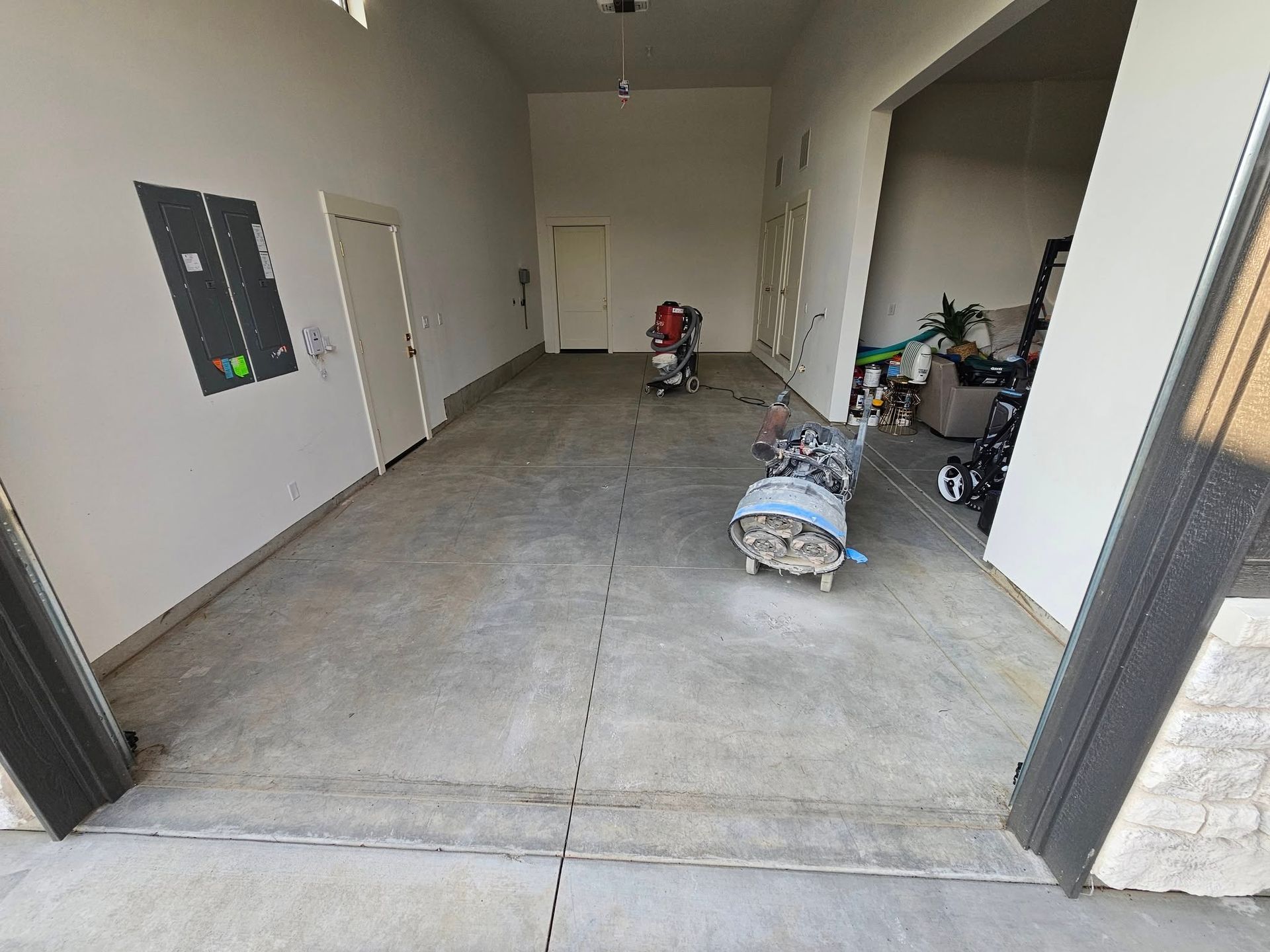Empty garage with concrete floor, white walls, and construction materials scattered near the back wall.